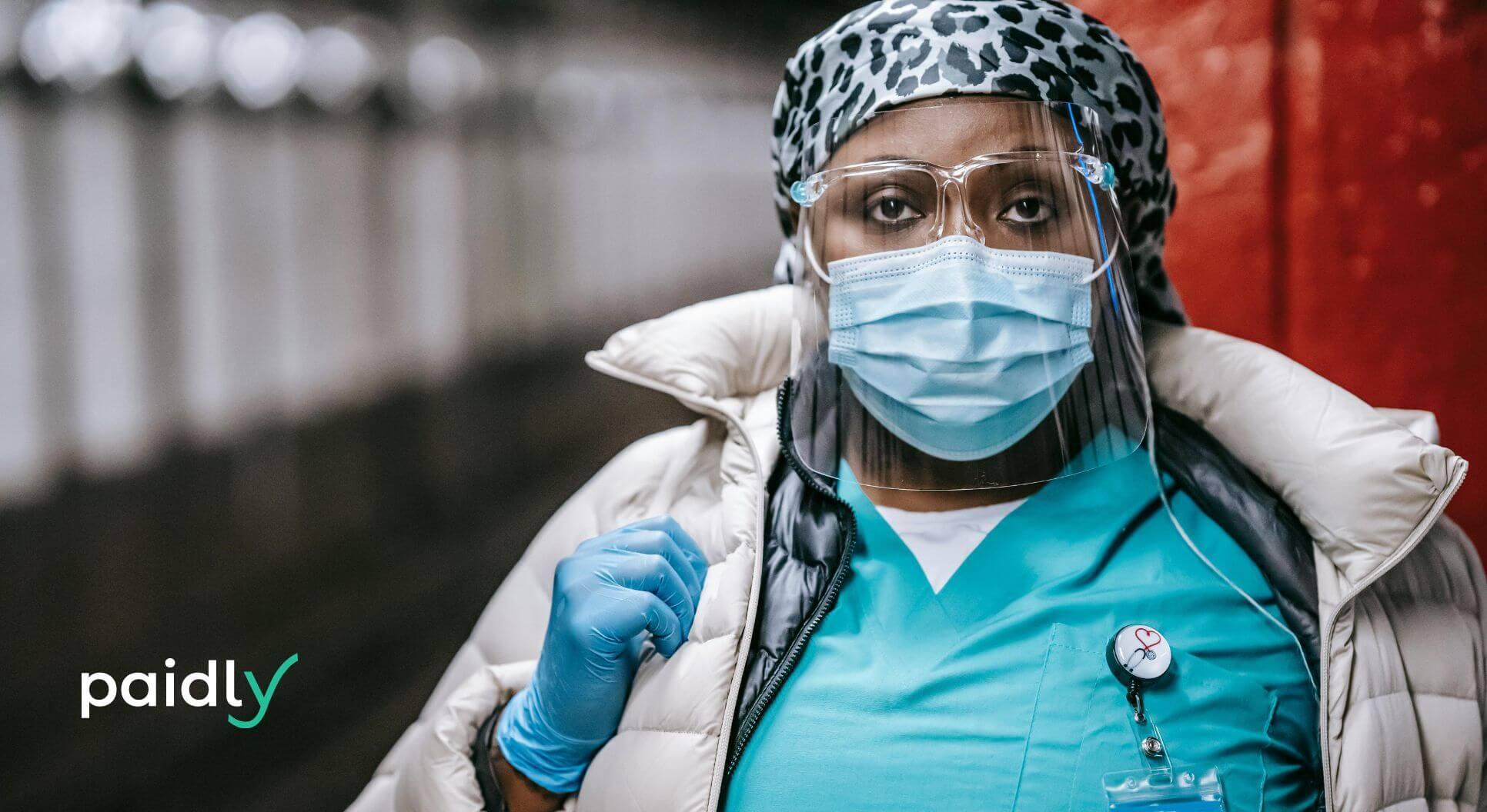 Serious black nurse in mask sanding on train platform