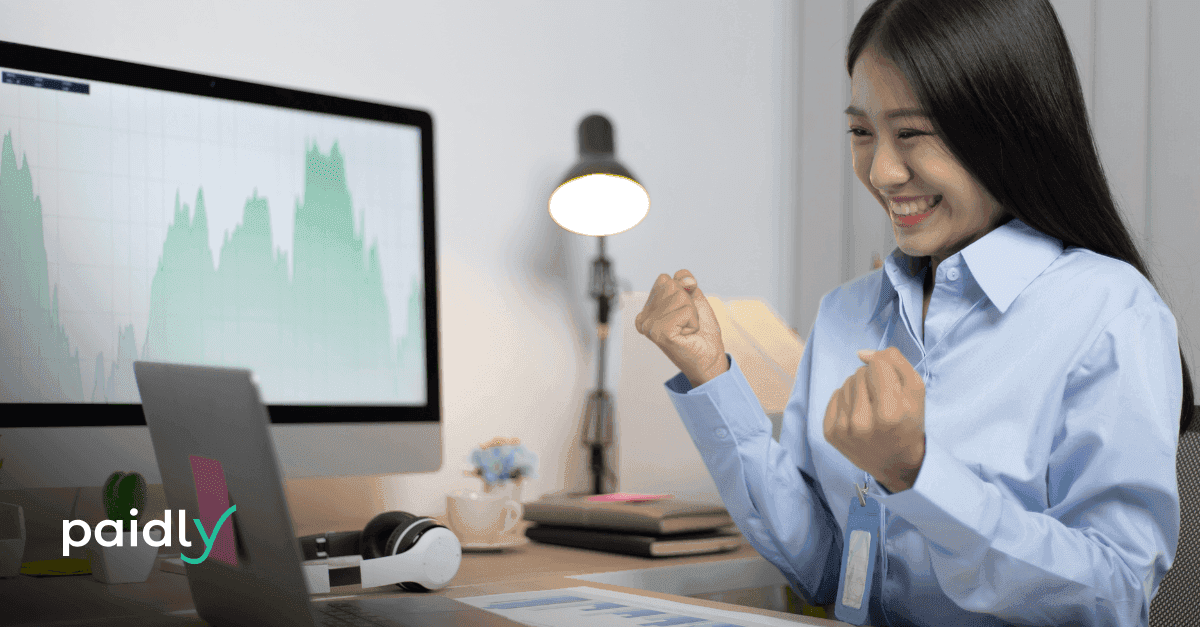 Maximizing Your Total Rewards Budget Employee celebrating as she looks at her work laptop, with the Paidly logo