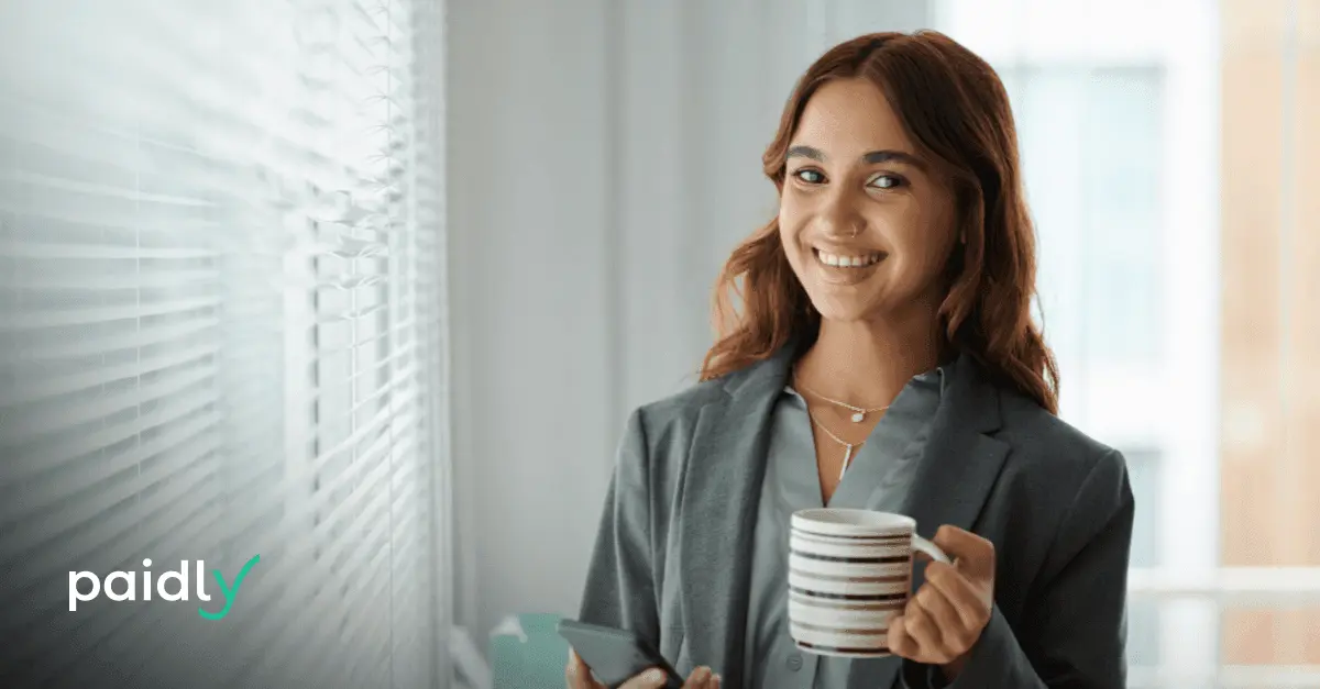 The HR Guide to Using Your Entire Education Budget HR employee holding a coffee mug and smiling at the camera, with the Paidly logo